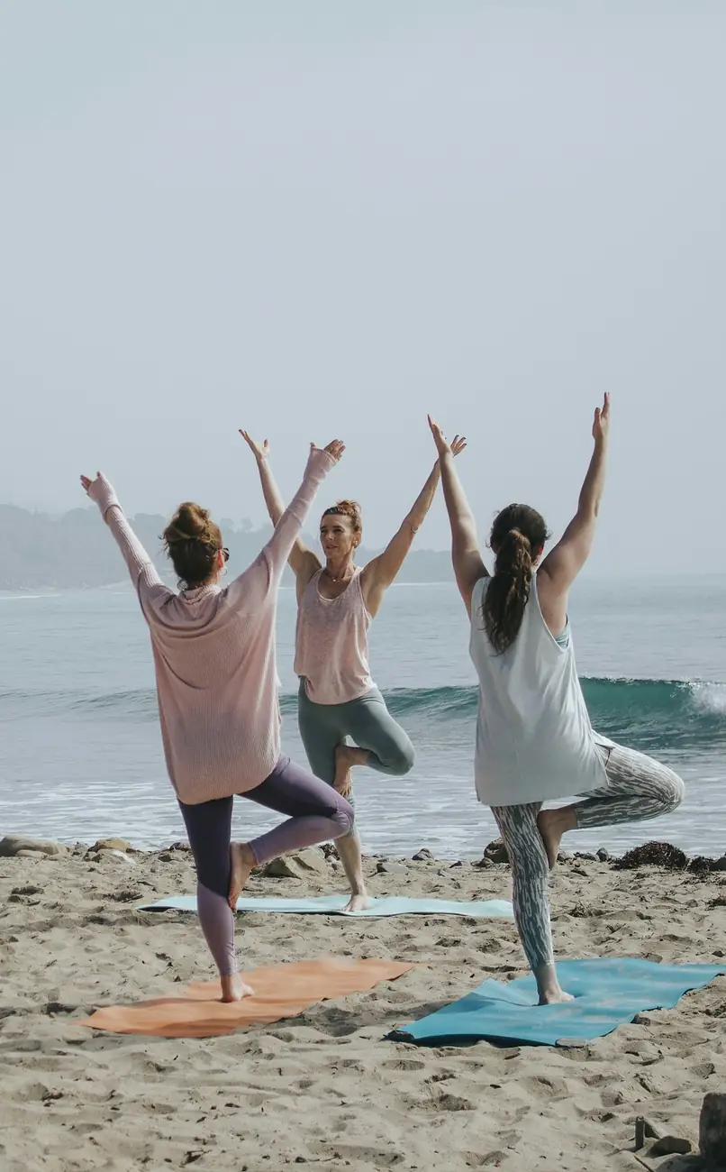 Three people stretching on a beach beside the water