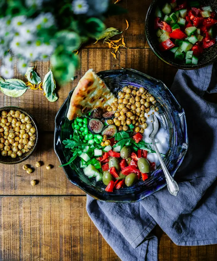 Bowl of chickpeas, vegetables and flatbread on a wooden table