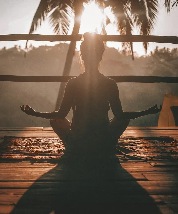 Person sitting cross-legged on a deck at sunrise