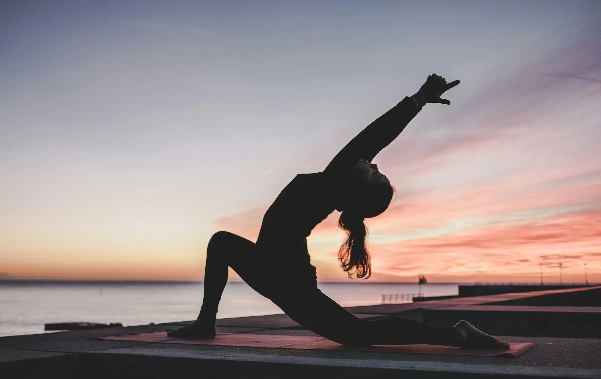 Person stretching beside the water at sunset